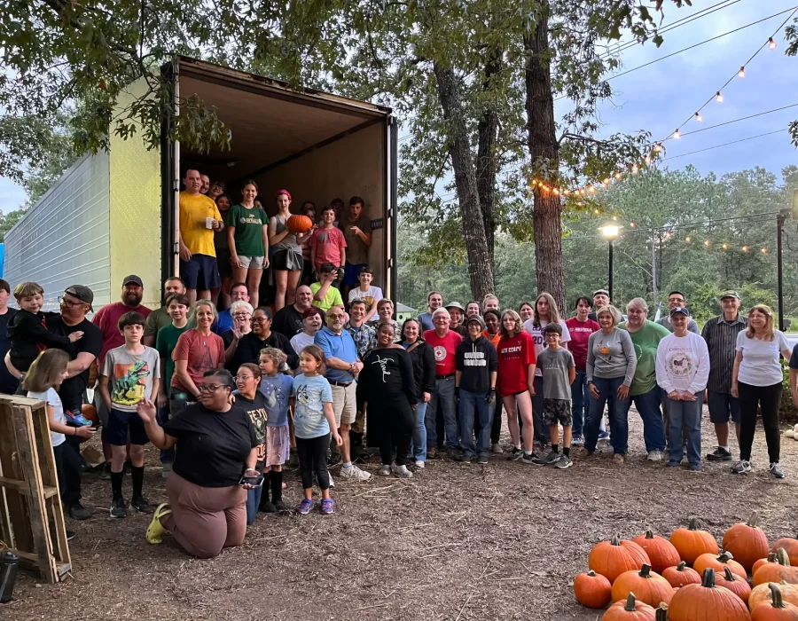 A large group of pumpkin patch volunteers pose for a photo, with an unloaded truck behind them.