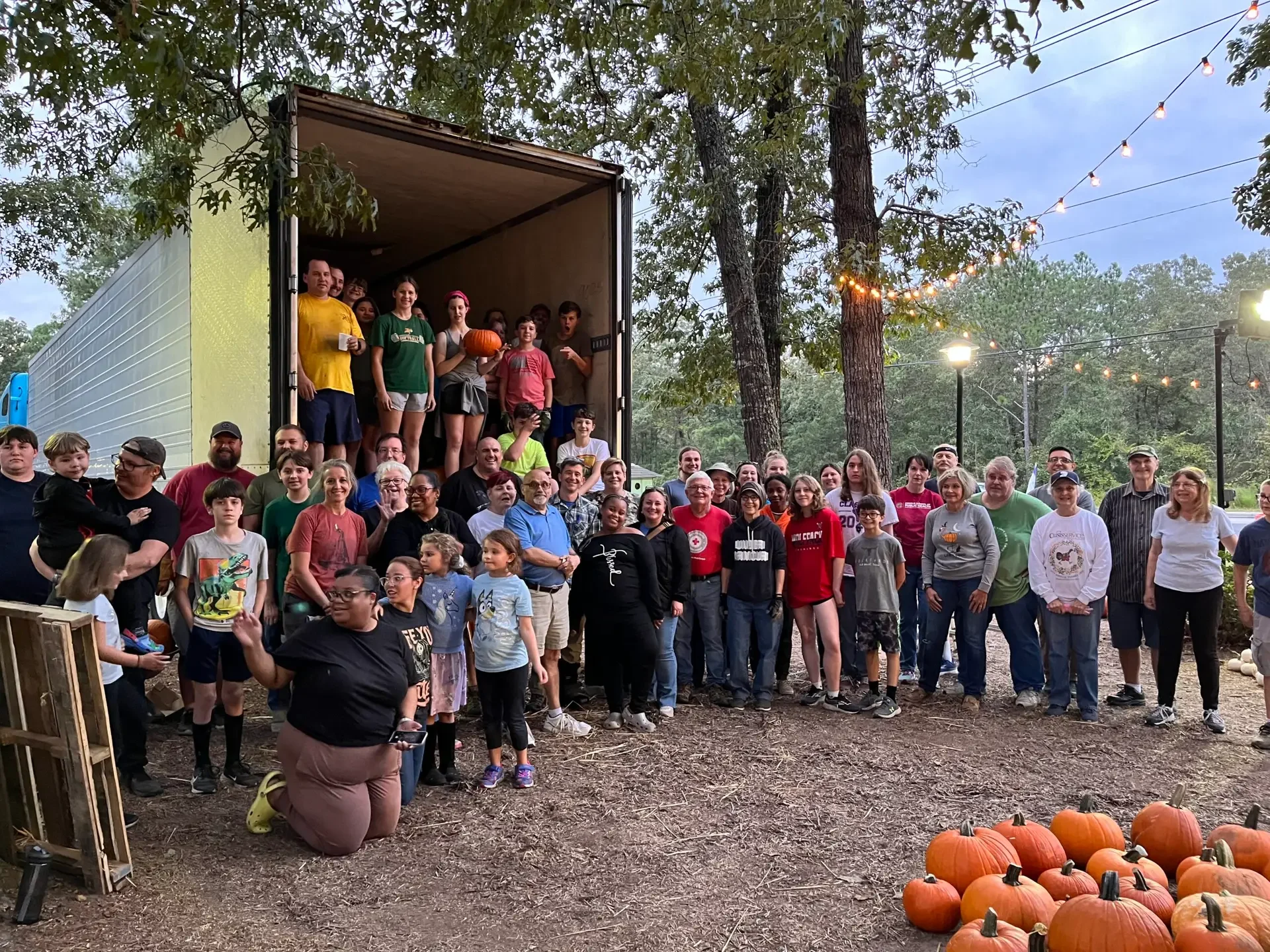 A large group of pumpkin patch volunteers pose for a photo, with an unloaded truck behind them.