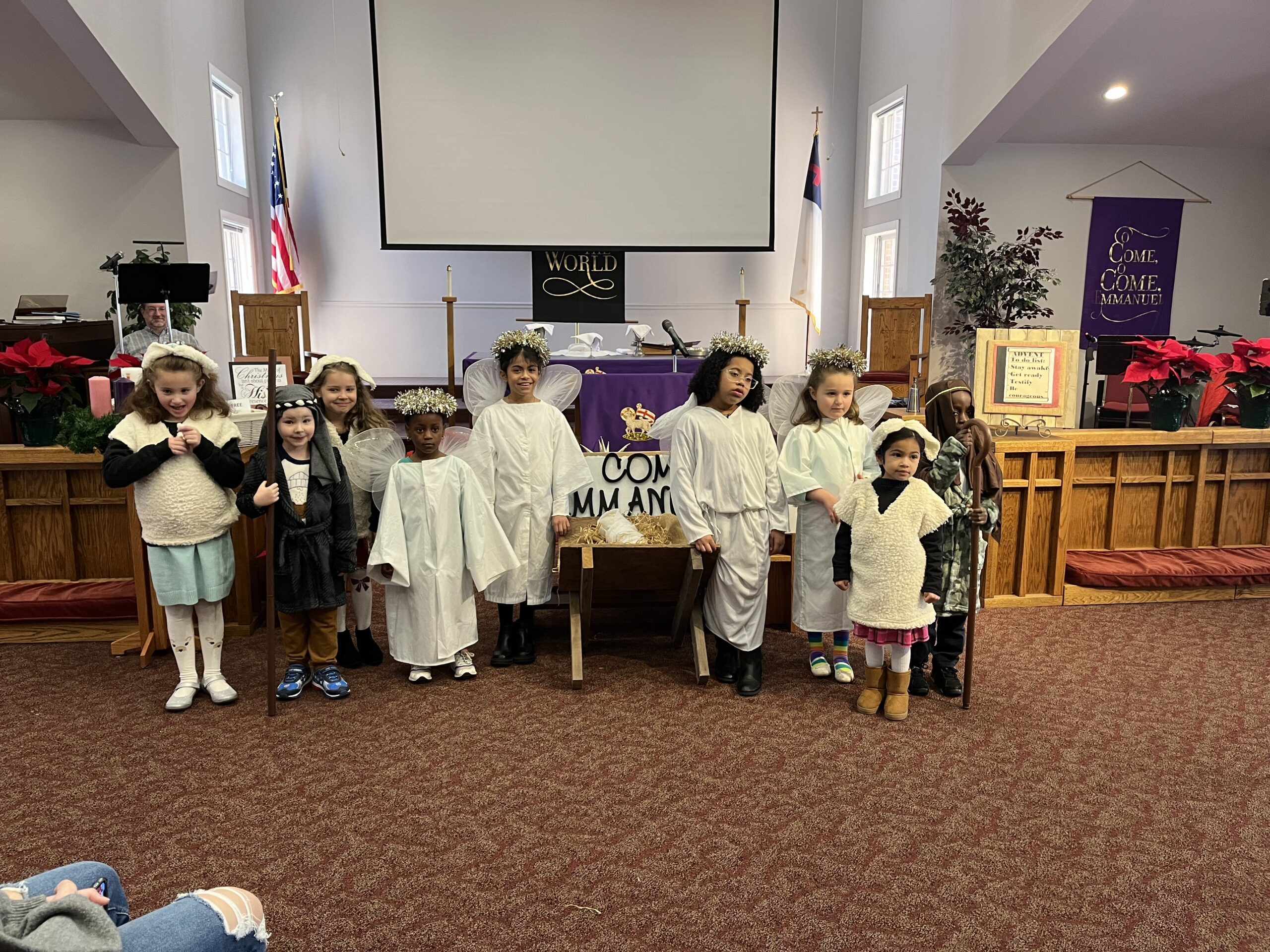 A group of children, dressed in angel and shepherd costumes, poses for a photo in the sanctuary